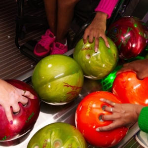 Hands reaching for different weight bowling balls on rack